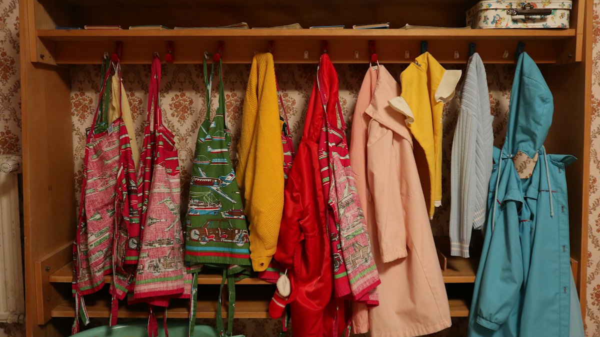 Garderobe einer Kita mit bunten Kinderjacken an Holzhaken