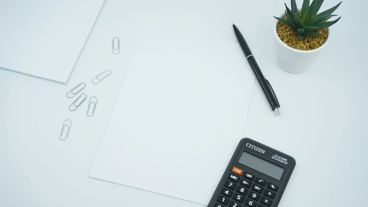 Taschenrechner, Stift und ein leeres Blatt Papier auf einem weißen Schreibtisch